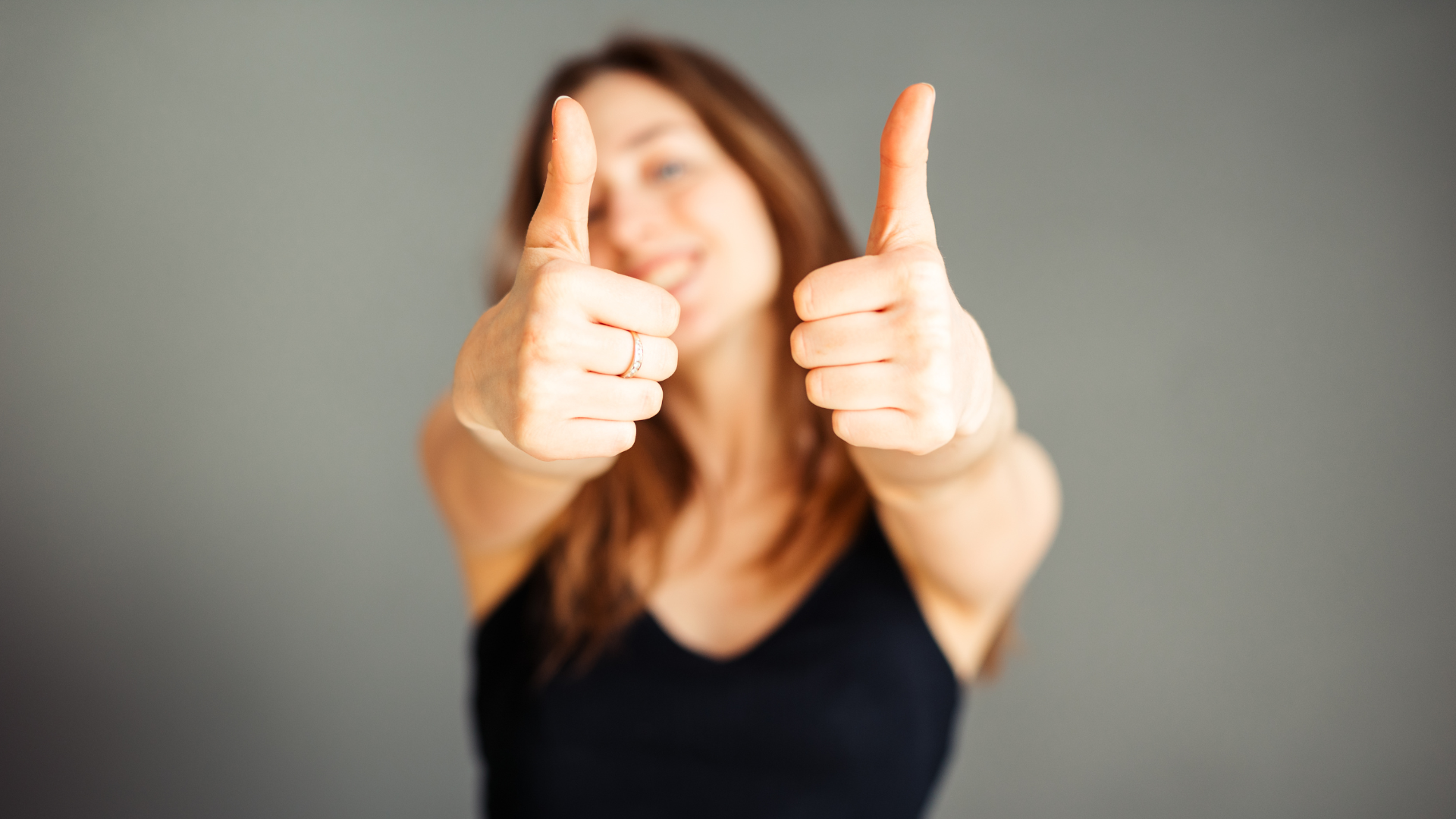 young girl in a black tank top holding her thumbs up smiling