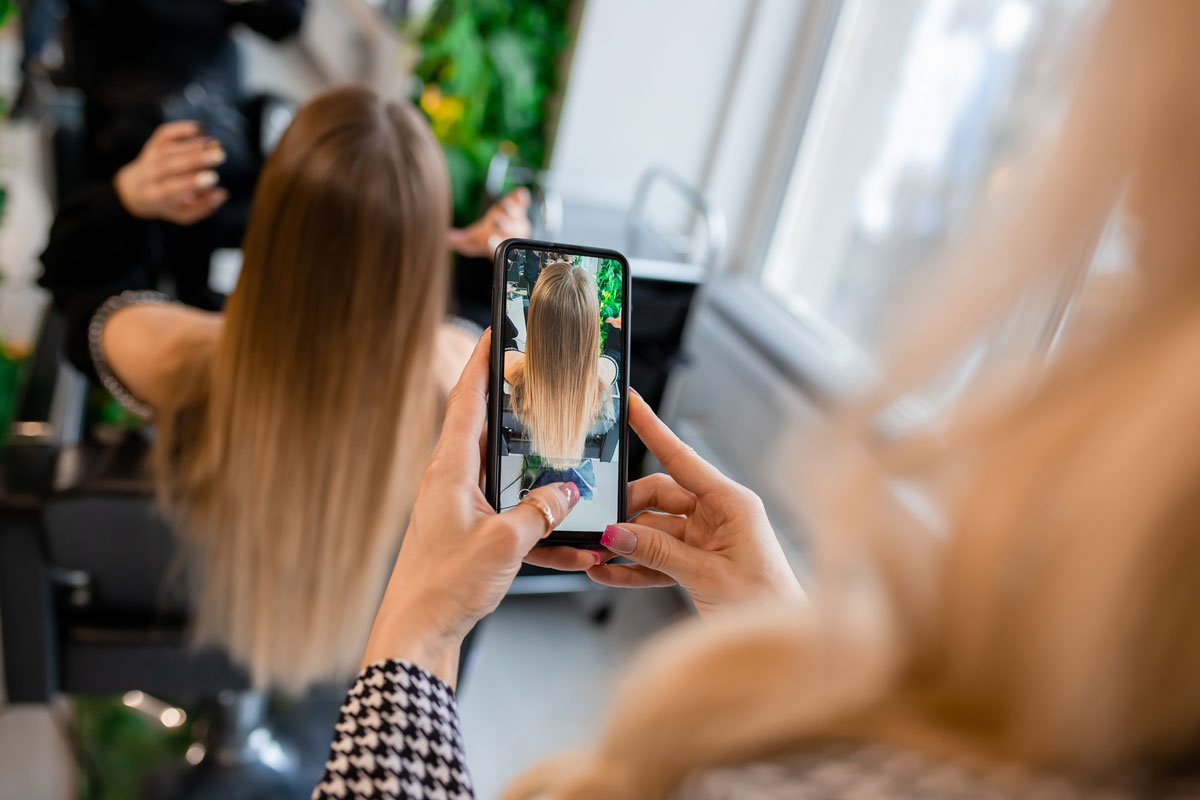A hairstylist takes a photo of her client’s hair for social media